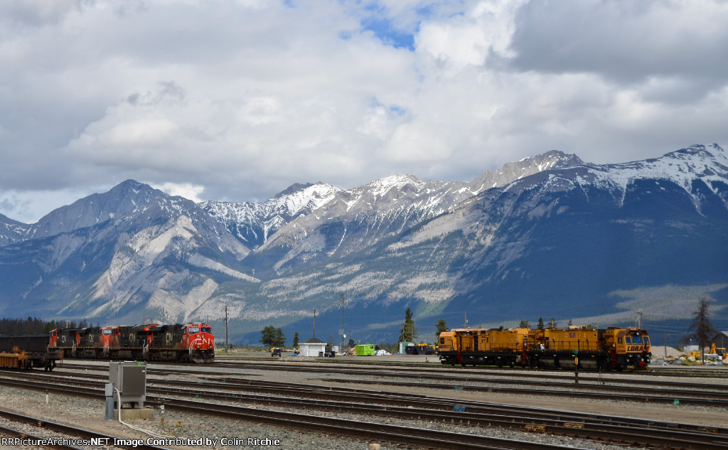 CN Jasper Yard, looking southeast towards the South Jasper Range, part of the Rockies, with W/B long, unit tank car train(3 hoppers separate the tank cars from the 4 CN locomotives, led by CN 3832.)